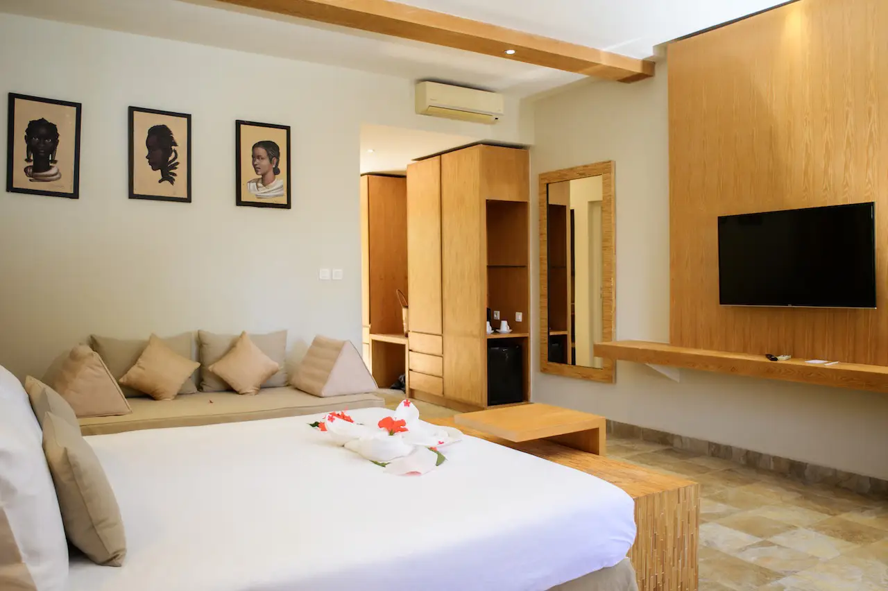 Hotel room with bed, sofa, wooden furniture, wall-mounted TV, and framed artwork on the wall.