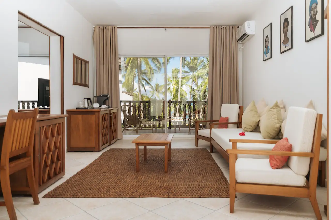 Living room with wooden furniture, beige cushions, rug, and balcony view of palm trees.