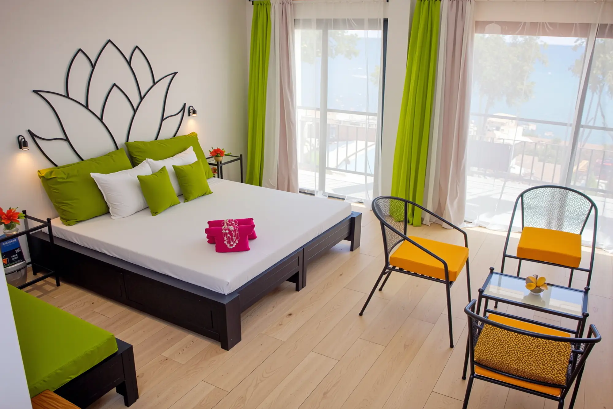 Modern bedroom with white bed, green pillows, yellow chairs, large windows, and floral wall art.