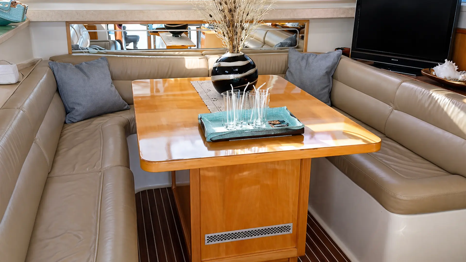 U-shaped beige leather bench seating around a wood table with glasses and a vase of dried plants.