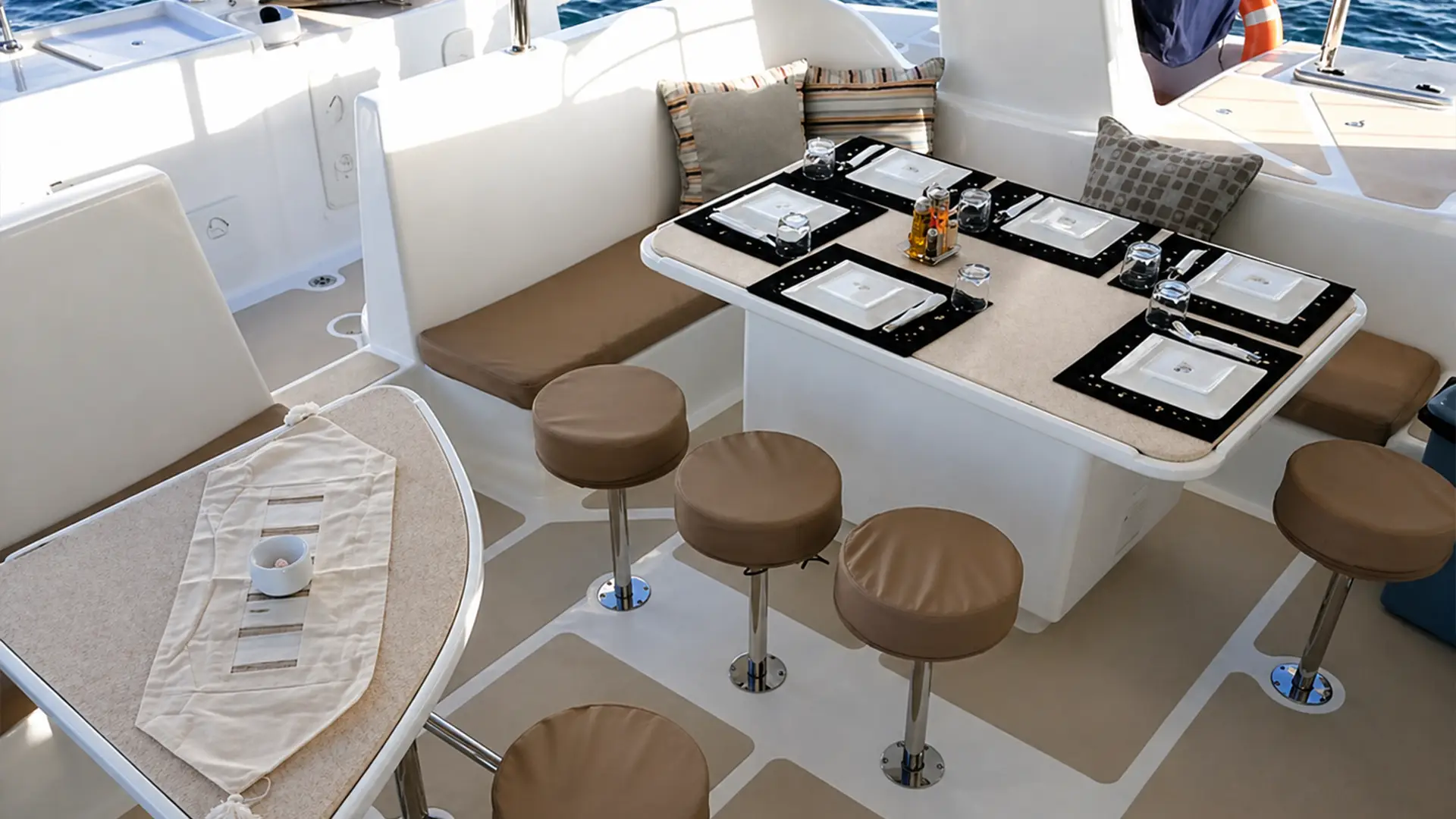 Boat dining area with beige cushioned stools, bench seating, and a table set for six with plates and glasses.