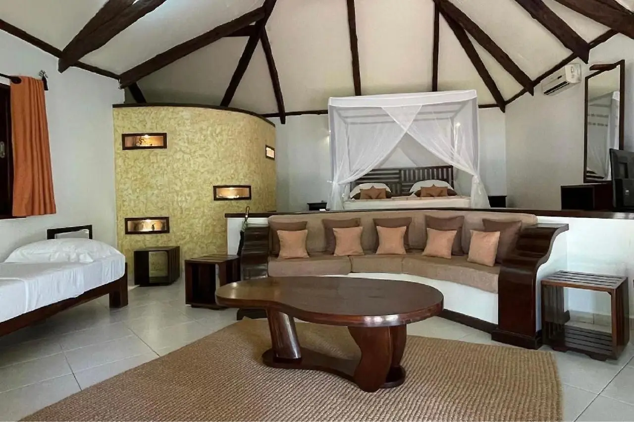 Room with beige curved sofa, brown wooden coffee table, canopy bed, and exposed ceiling beams.